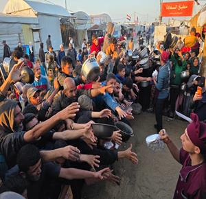 نازحون يتزاحمون للحصول على طعام مجاني من مطبخ خيري في اليوم الرابع من شهر رمضان المبارك في مواصي خان يونس جنوب قطاع غزة